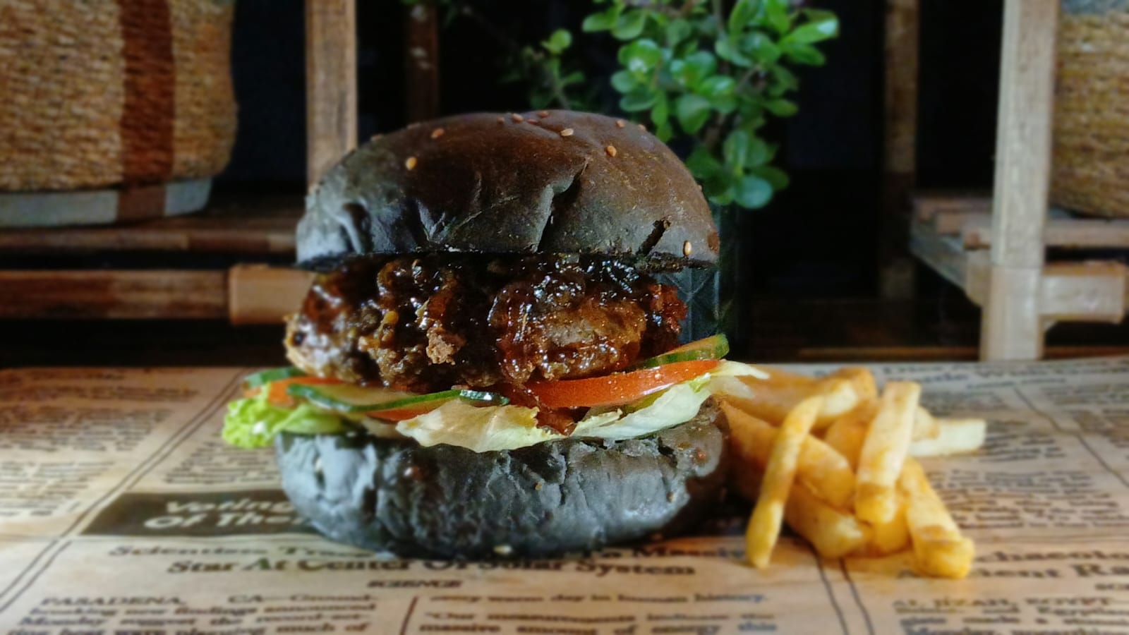A signature burger on a black bun with chips beside it