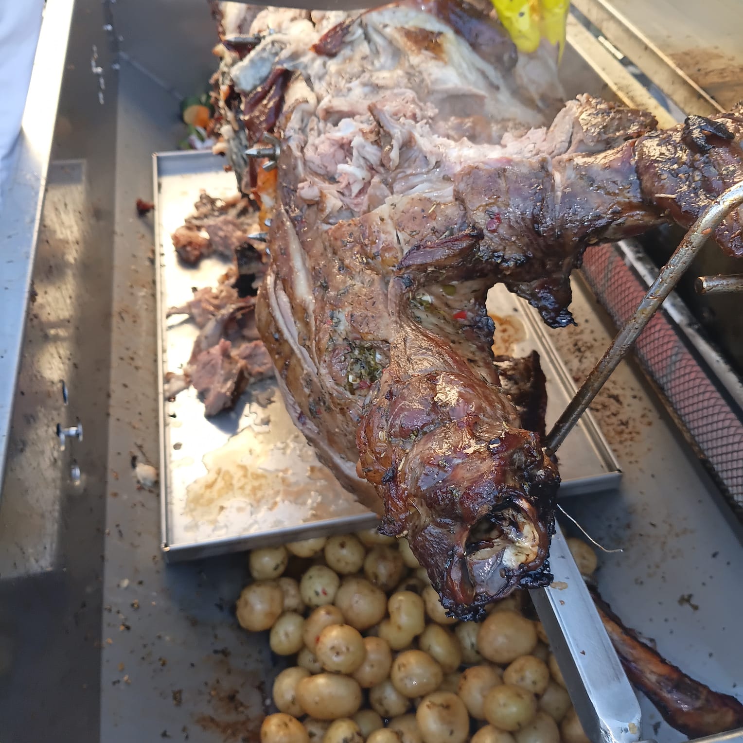 Spit-roasted lamb being carved, with roast baby potatoes in the tray