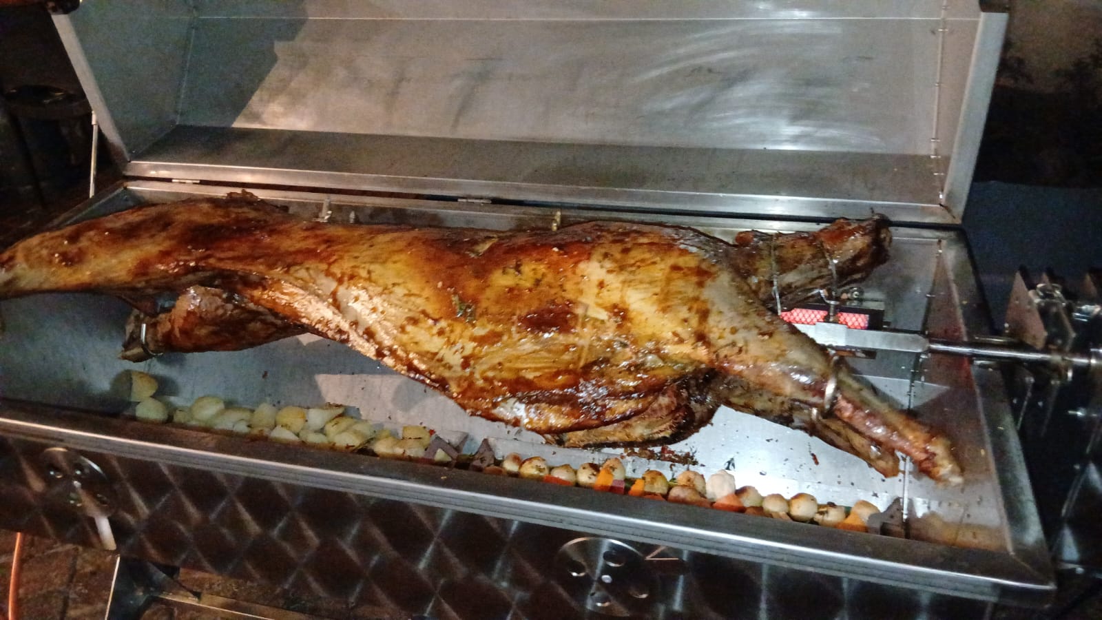 A whole lamb on the spit with roast baby potatoes and baby onions in the tray