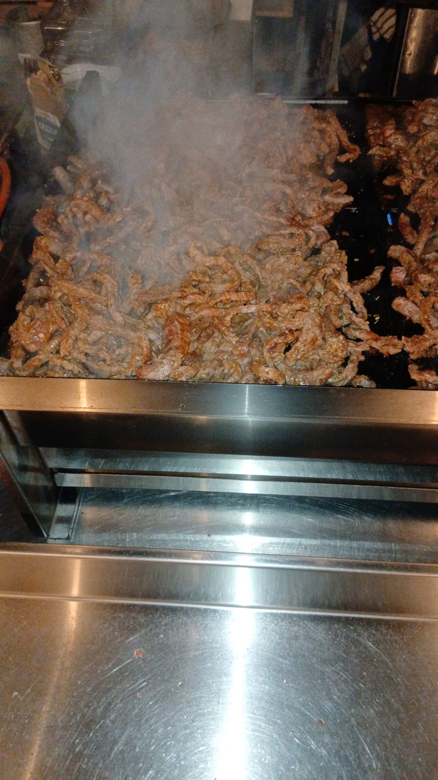Strips of steak sizzling on the flat-top grill