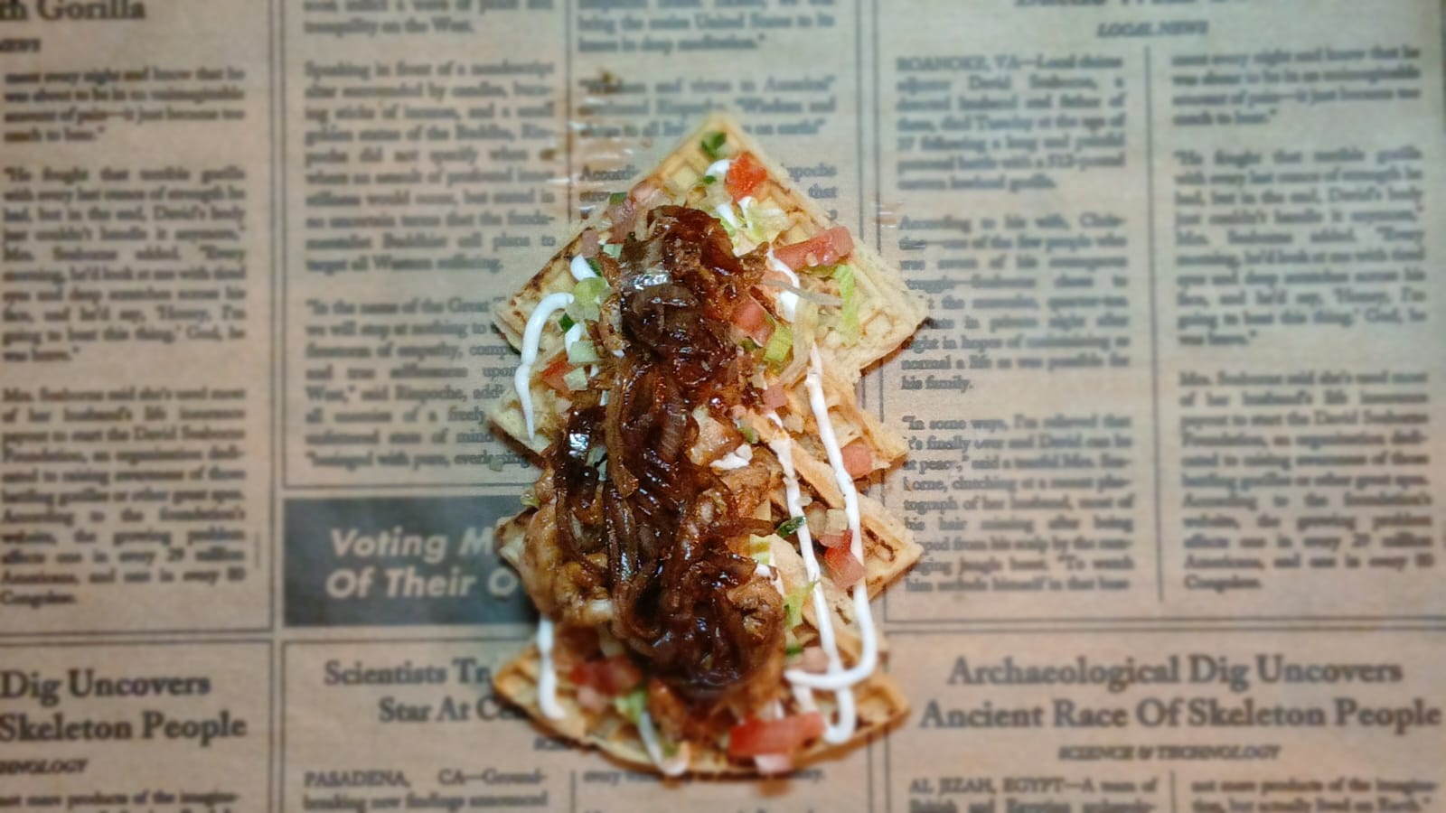 A stacked waffle meal with steak, caramelised onions, salsa and sauce, seen from above